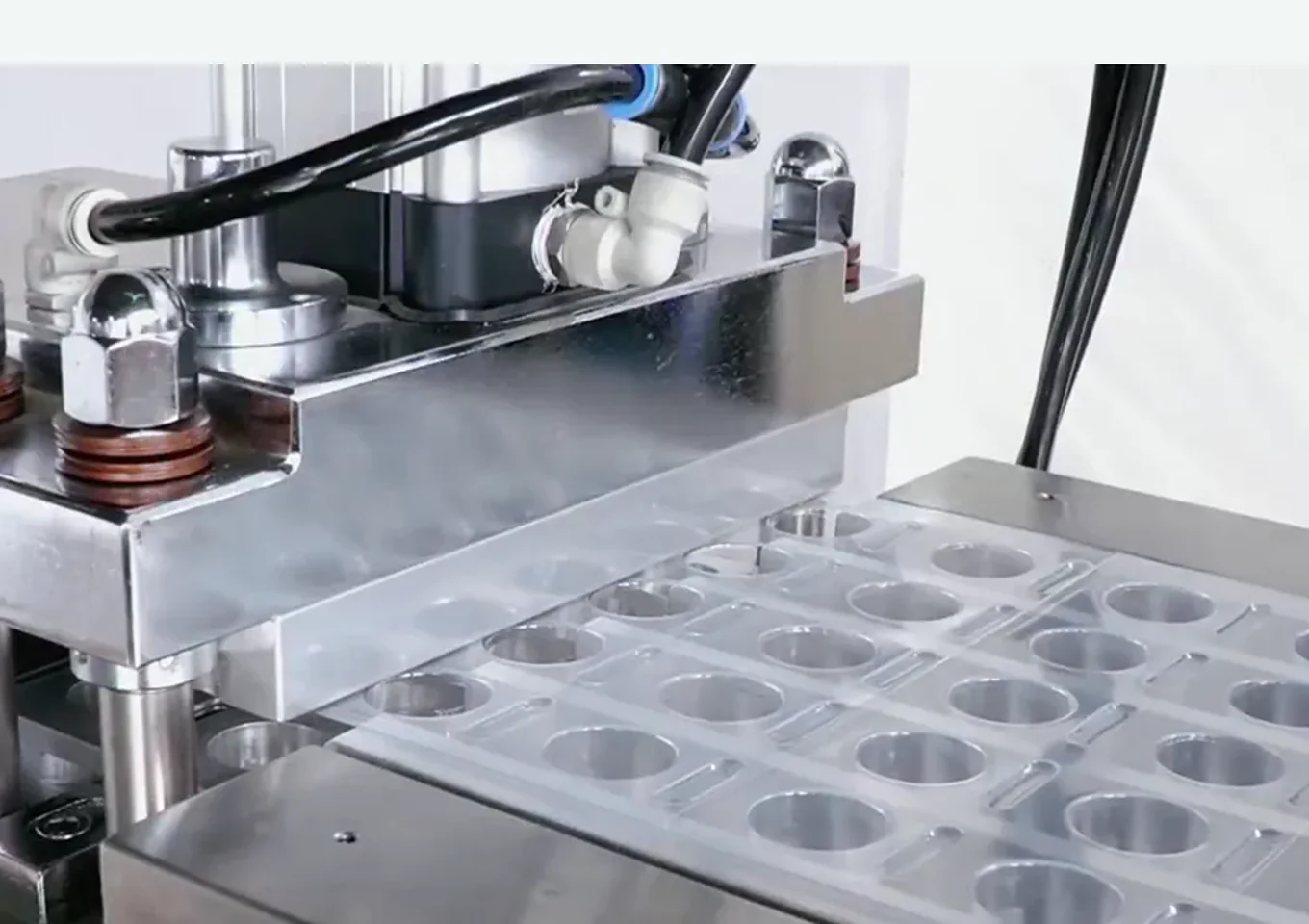 Close-up of equipment showing transparent sheet being heated and formed into multiple blister cavities