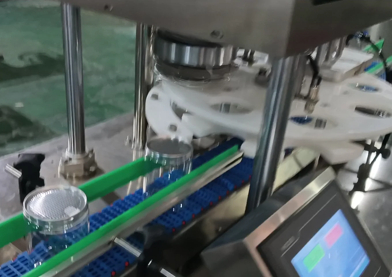 Close-up of transparent can body and lid entering the white indexer and below the seaming head along the conveyor belt