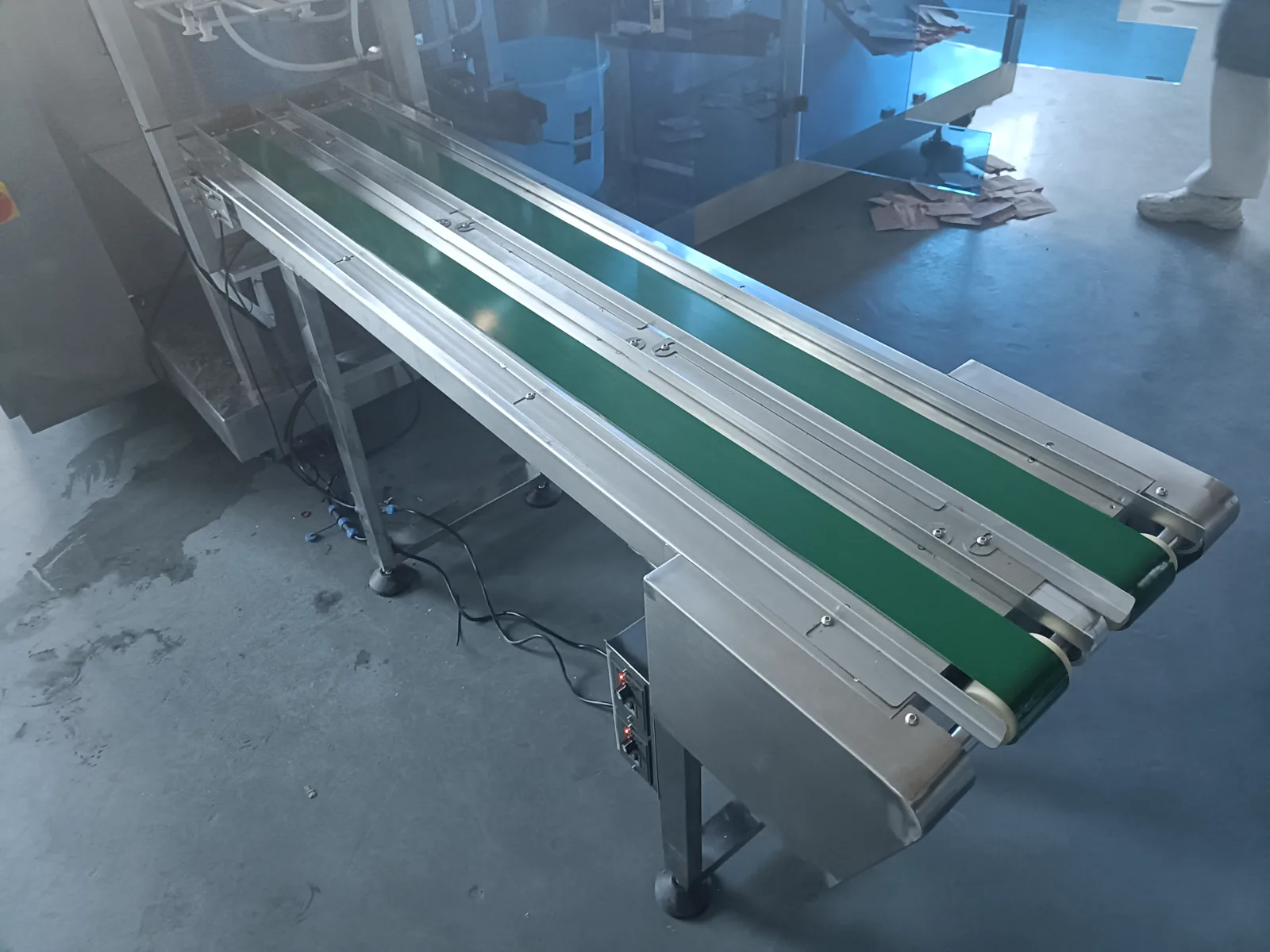 Close-up of the discharge end of a dual-lane packaging machine with two parallel green conveyor belts