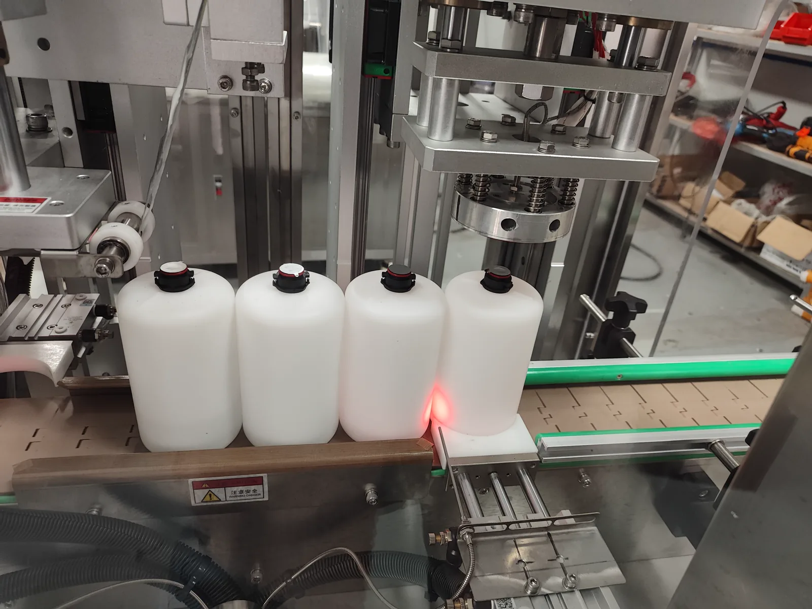 Close-up of station with white bottles/jars aligned under sensor positioning and die-cut sealing head