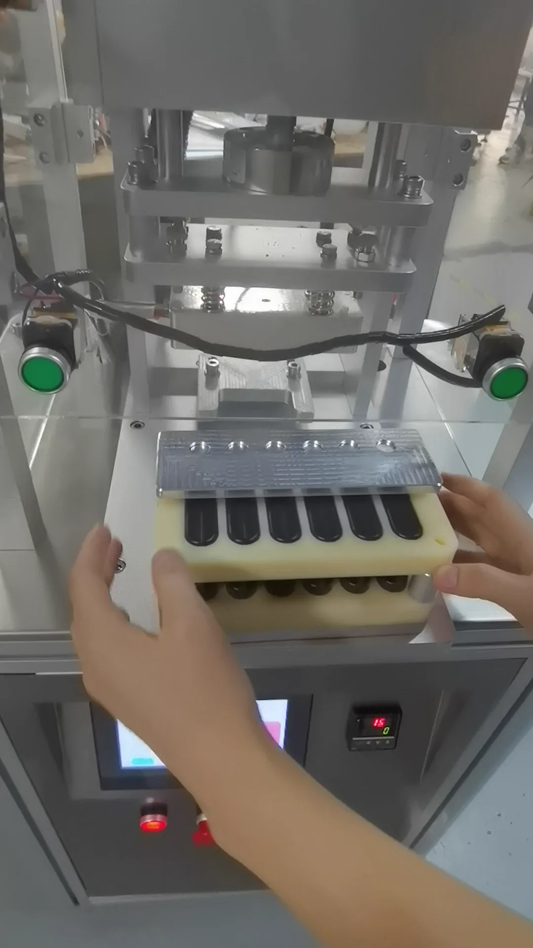 Operator feeding a carrier with six black test pieces into the multi-cavity sealing press area